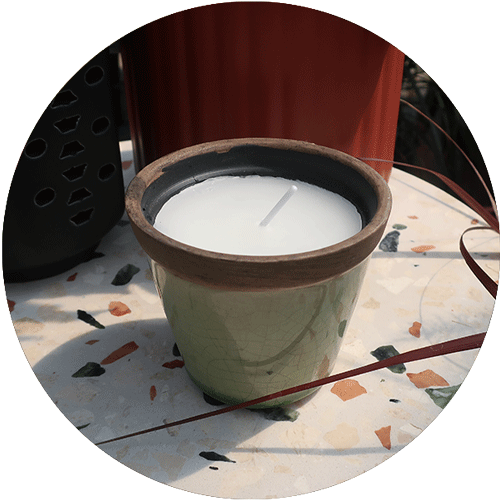 A small citronella candle sitting on a plant stand.